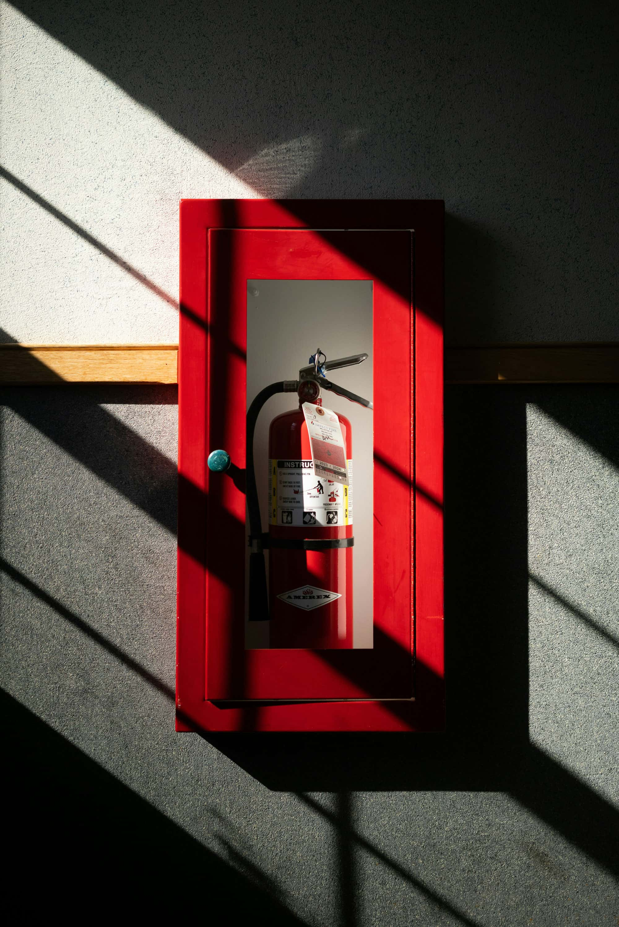 Roter Feuerlöscher in einem Wandkasten, beleuchtet durch Sonnenstrahlen.