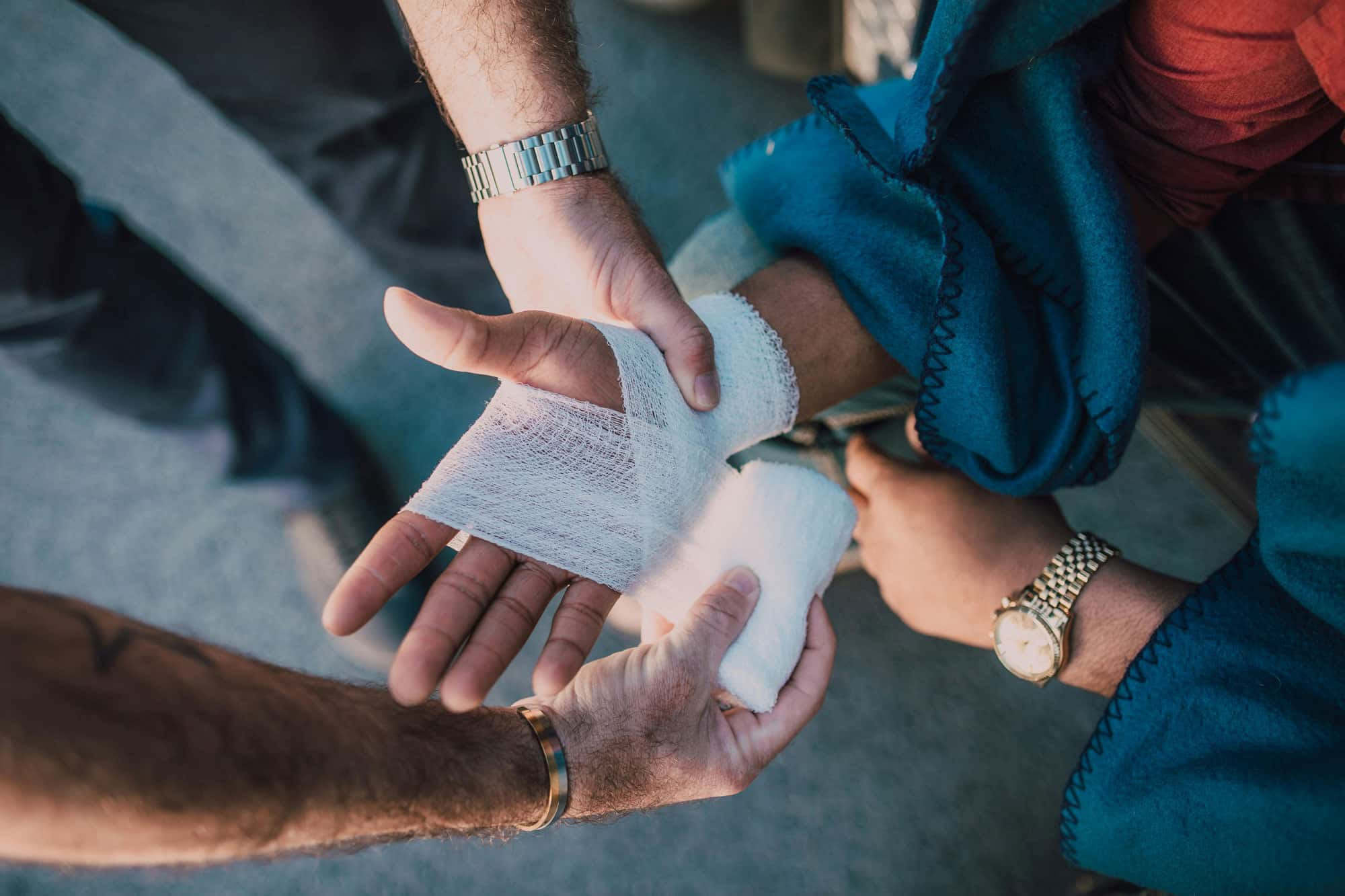 Hand wird mit einer Bandage versorgt, während eine andere Person beim Anlegen des Verbands hilft.