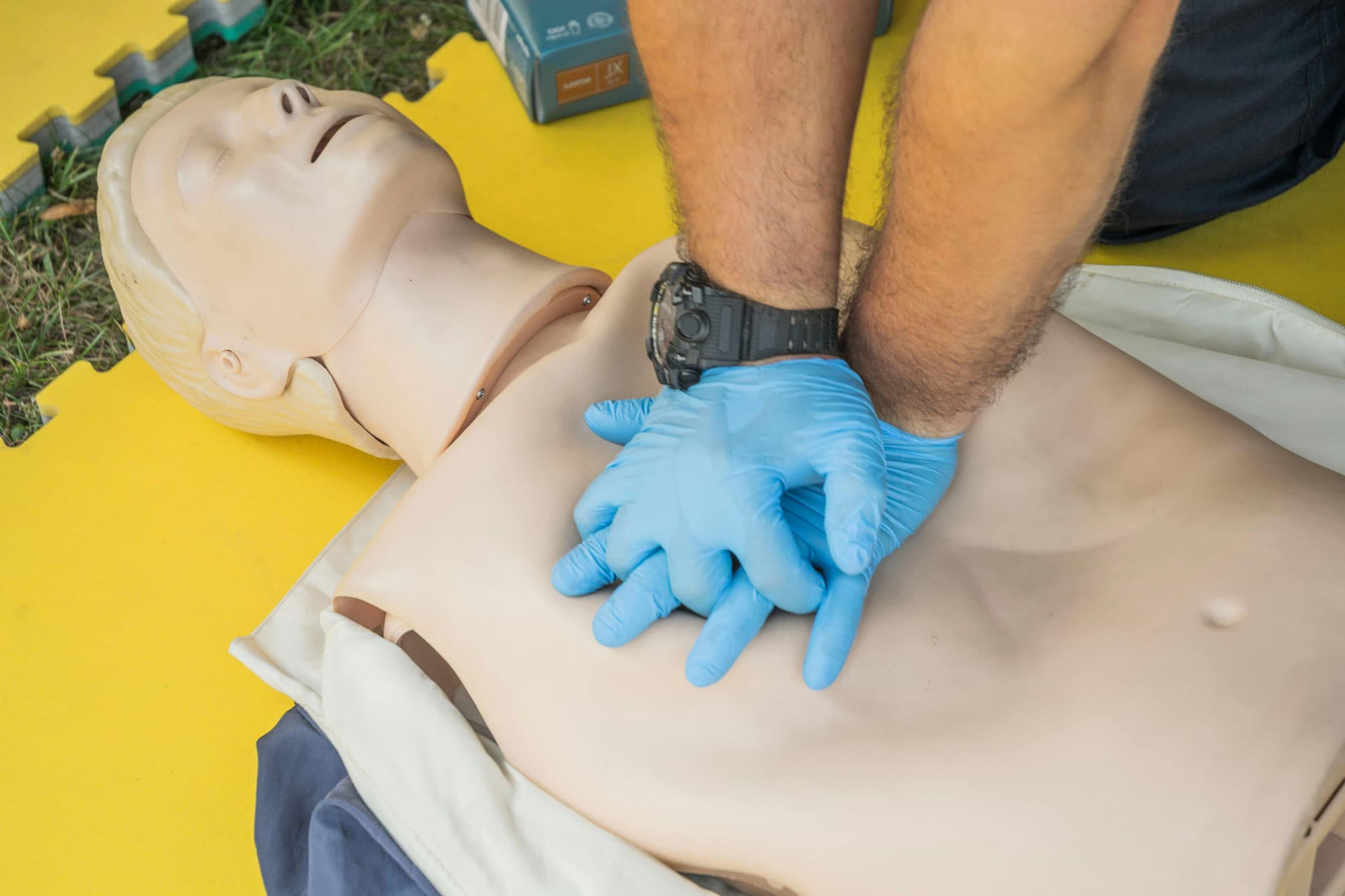 Person übt eine Herz-Druck-Massage an einer Wiederbelebungspuppe mit blauen Handschuhen.