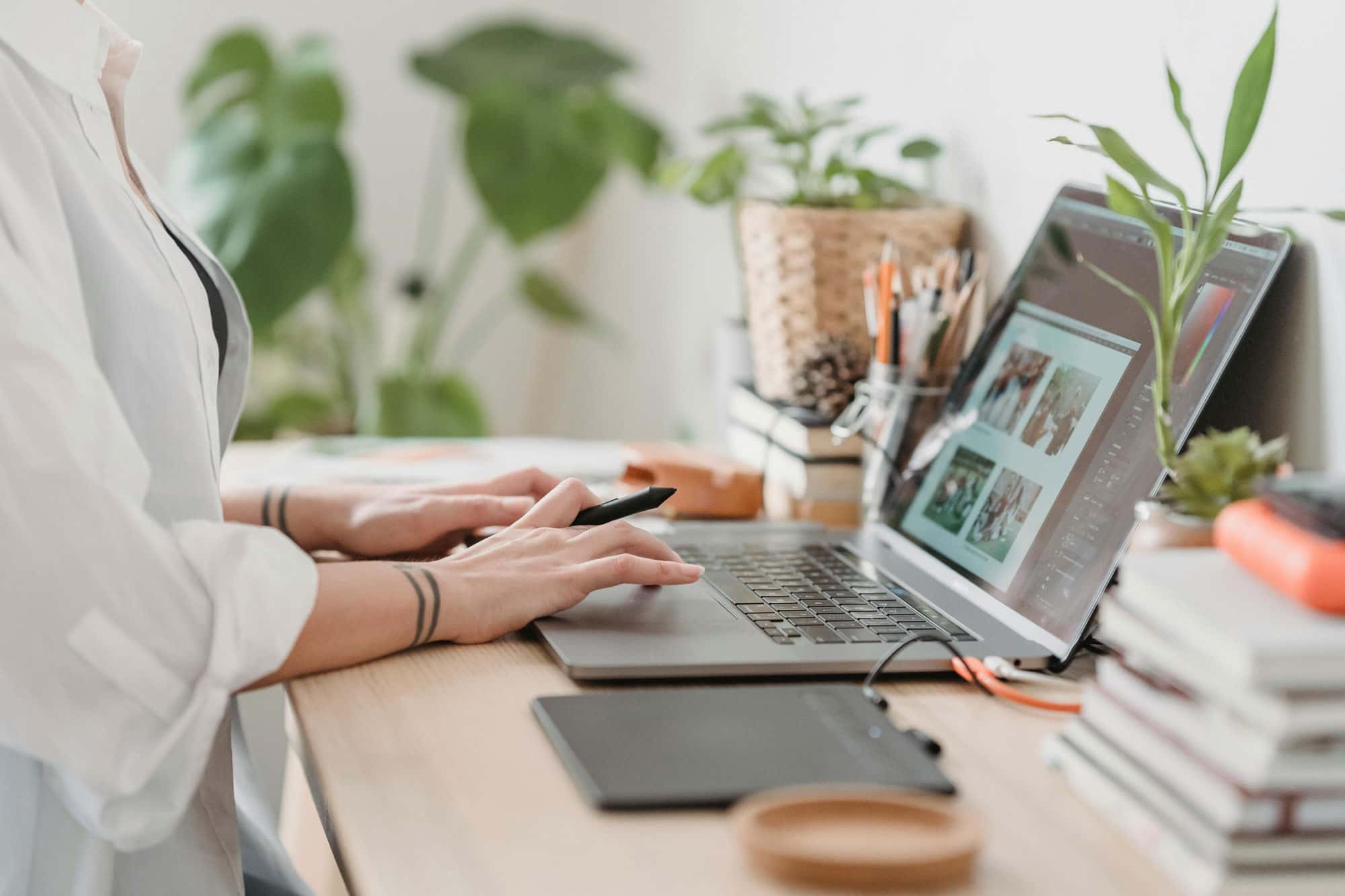 Person arbeitet an einem Laptop in einem modernen, gemütlichen Home-Office mit Pflanzen und Büromaterialien im Hintergrund.
