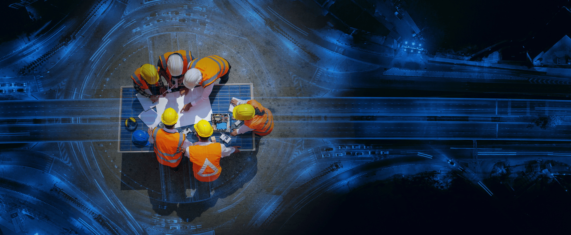 Das Bild zeigt eine Gruppe von Bauarbeitern in orangefarbenen Schutzwesten und Helmen, die um einen Tisch stehen und Pläne besprechen